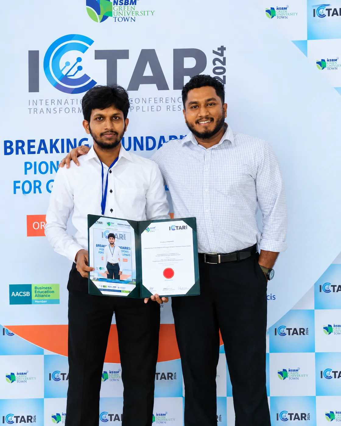 Pasindu Sandamal holding the ICTAR certificate beside the research supervisor, in front of the ICTAR 2024 backdrop.